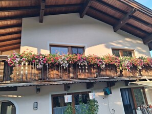 A building with a balcony adorned with flowers, wooden beams, and a window. - Apartment "Haus Wildenbach" with Mountain View, Private Terrace and Wi-Fi (Niederau)