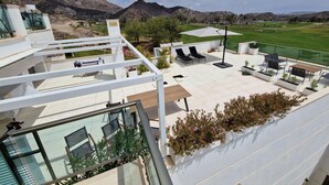 Terraza en la azotea con mobiliario exterior, piscina y vistas a un campo de golf y montañas.