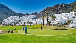Un campo de golf con montañas al fondo y edificios blancos.
