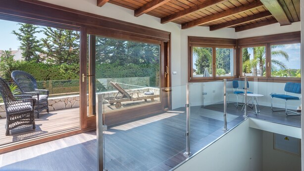 Een moderne kamer met een houten plafond, grote schuifdeuren en een balkon met tuinmeubilair.
