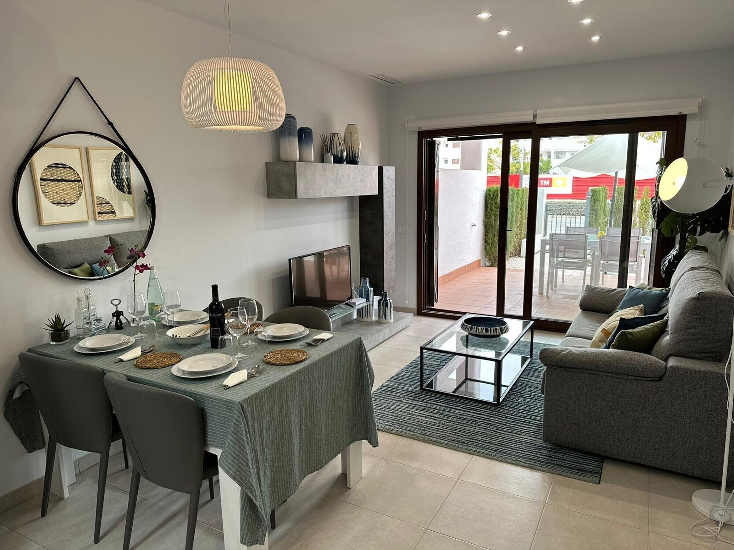 Una sala de estar moderna con comedor, sofá, televisor y un amplio ventanal con vistas al exterior.