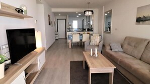 A modern living room with a flat-screen TV, a wooden coffee table, a sofa, and a dining area in the background. - Family apartment 3 bedrooms near beach (San Juan de los Terreros)