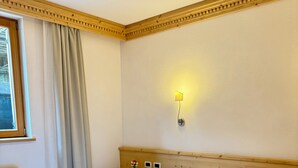 A double bed with white linens in a room with a wooden headboard, a nightstand with a lamp, and a window with curtains.