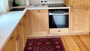 A kitchen with wooden cabinets, a white countertop, a red patterned rug, and a built-in oven.