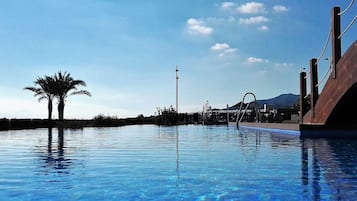 Una piscina azul cristalina con la silueta de una palmera, un puente metálico y una montaña al fondo.