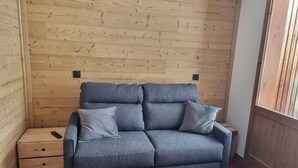 Ein graues Sofa mit zwei Kissen in einem Eckzimmer mit Holzwänden und einem roten Teppich.