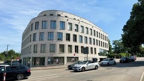 Ein modernes Gebäude mit einer geschwungenen Fassade, zahlreichen Fenstern und einem Parkplatz mit Autos.