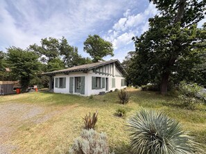 A small, single-story house with a tiled roof, surrounded by a grassy yard and various plants. - Modern villa in Grand-Piquey near Arcachon Basin, capacity for 7 people (Lège-Cap-Ferret)