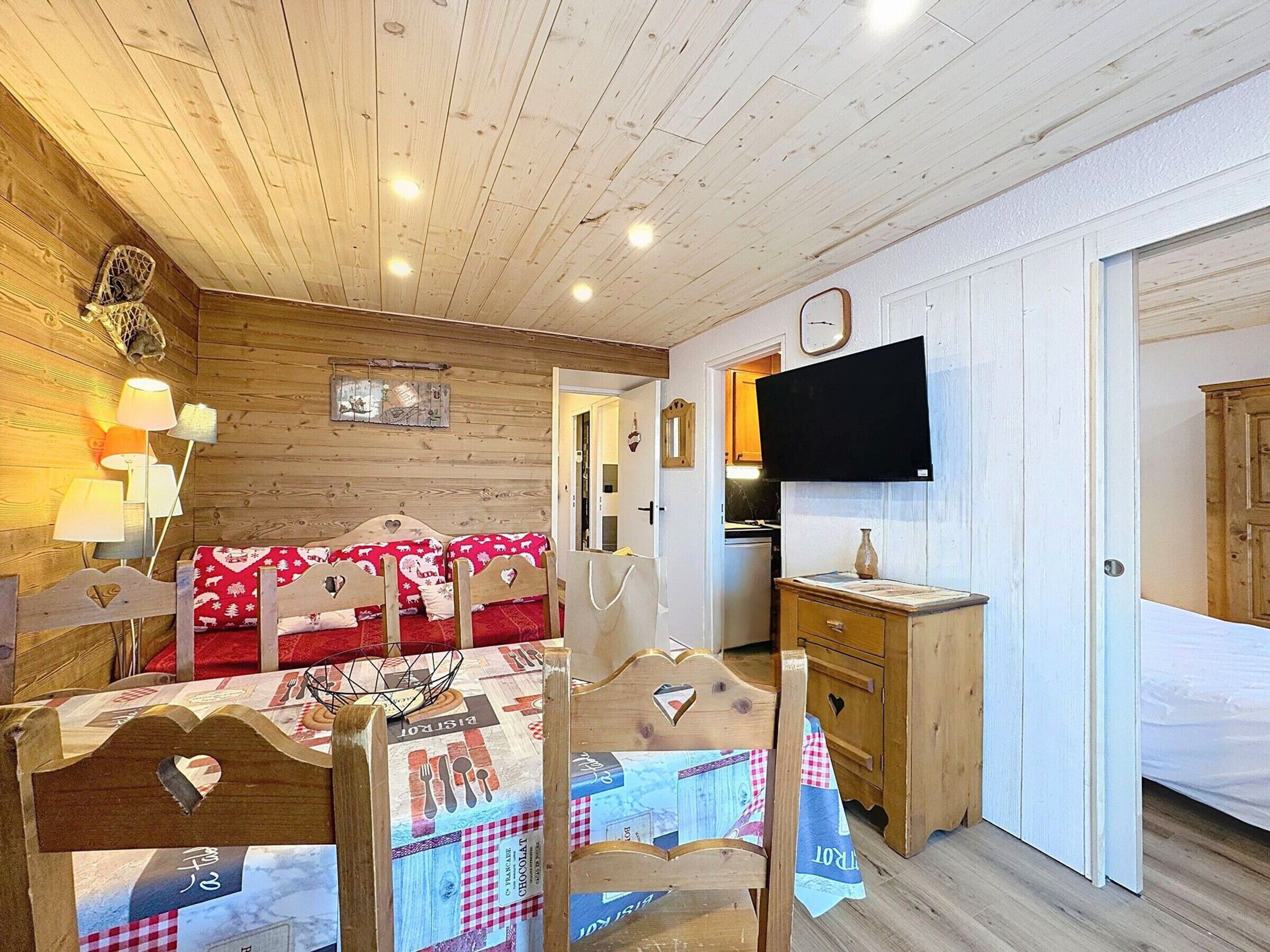 A cozy room with a wooden ceiling, a bed with heart-shaped headboards, a dining table with a placemat, a TV mounted on the wall, and a wooden cabinet.