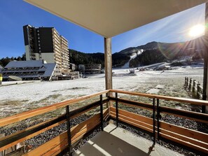 Un balcó amb vista a un paisatge nevàt, un edifici i una muntanya al fons.