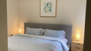 Ein ordentlich bezogenes Bett mit gestreifter Bettwäsche, einem grauen Kopfteil und zwei Nachttischlampen.
