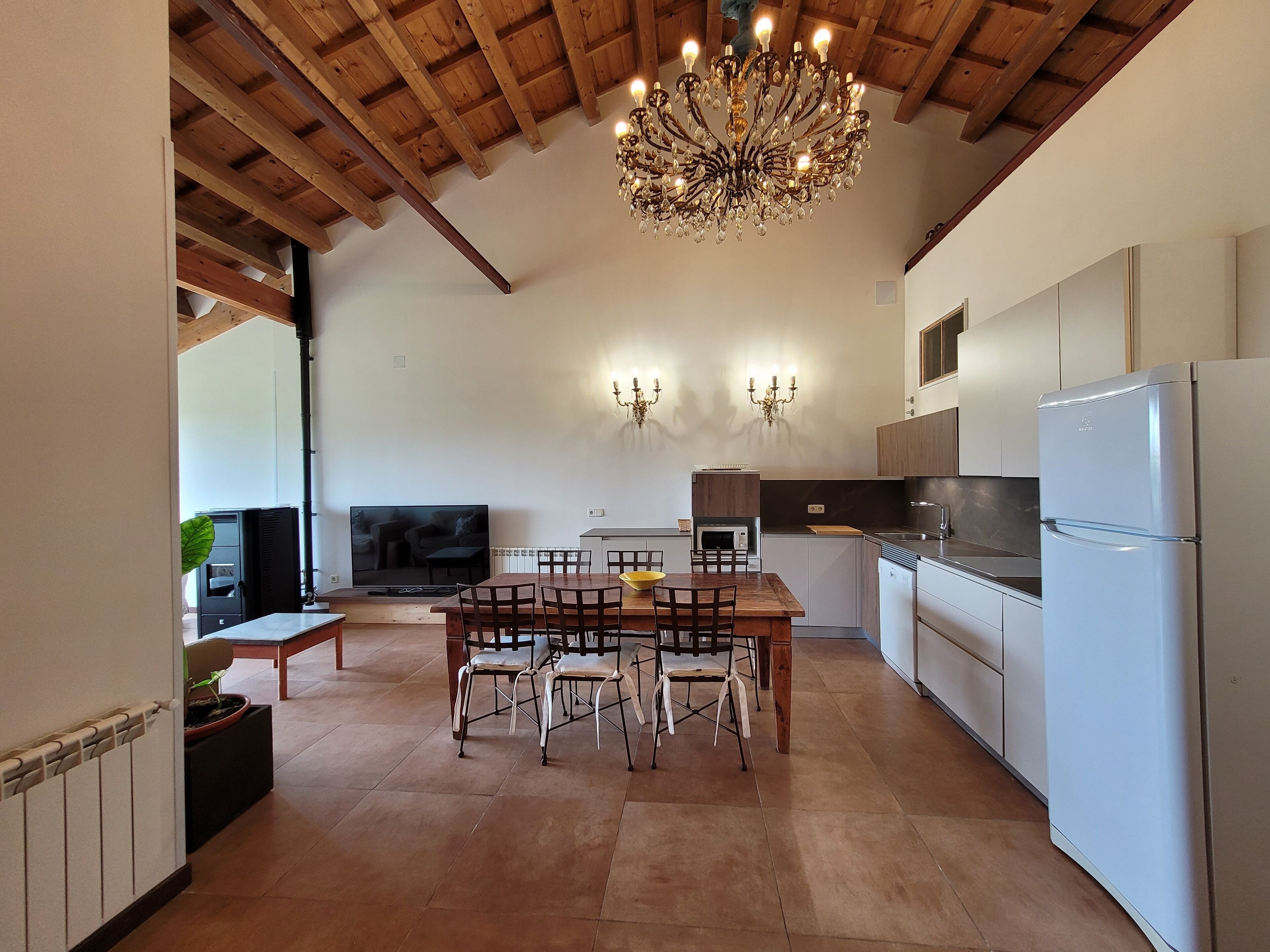 A modern kitchen with a dining area, wooden ceiling beams, and a chandelier.