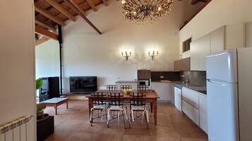A modern kitchen with a dining area, wooden ceiling beams, and a chandelier.
