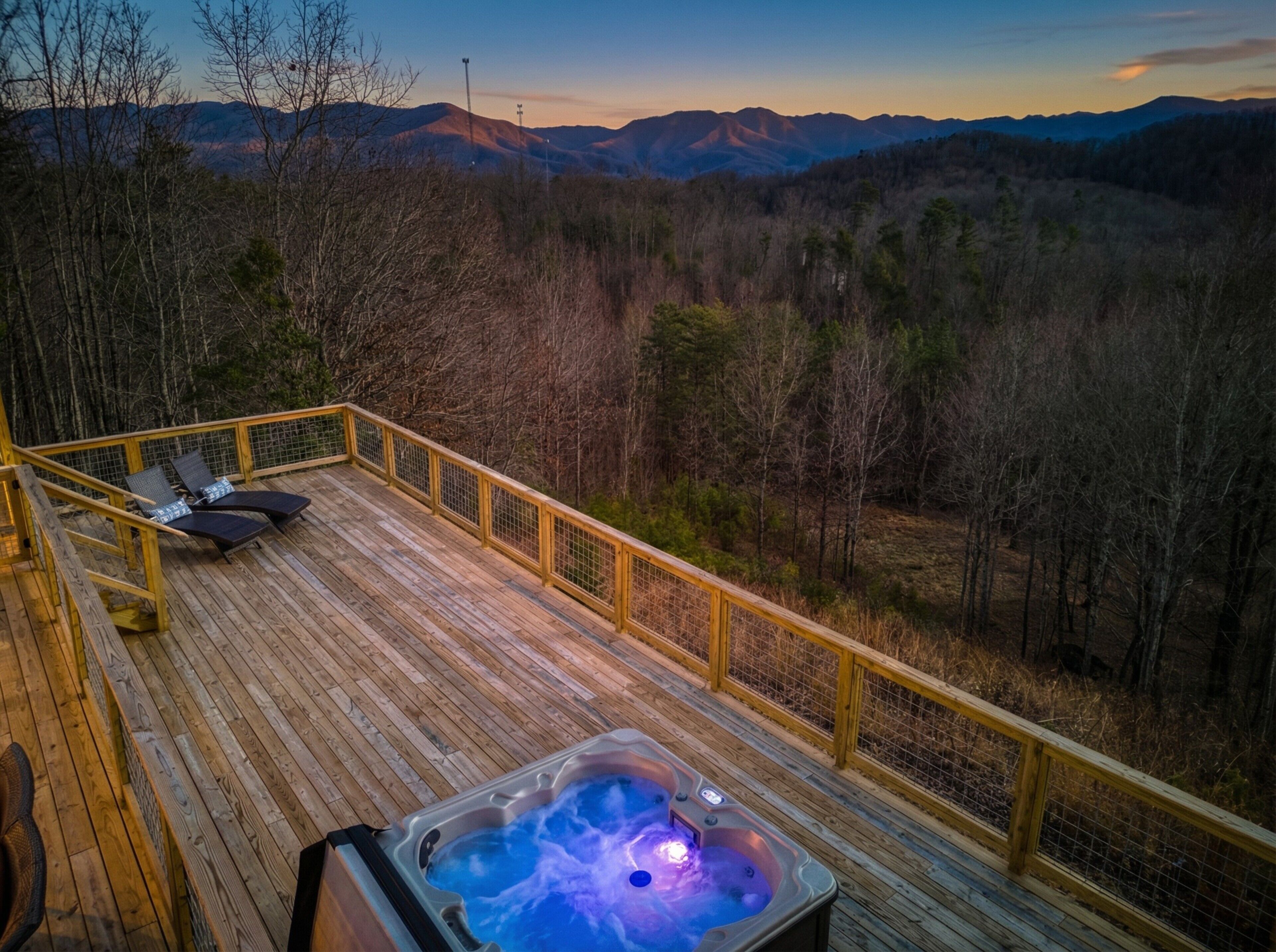 Eine Holzterrasse mit Whirlpool und Liegestühlen mit Blick auf eine gebirgige Landschaft.