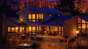 Een houten chalet met twee verdiepingen, grote ramen, een terras en een hottub.