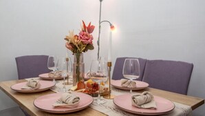 Een eettafel gedekt met roze borden, glazen en een vaas met bloemen.