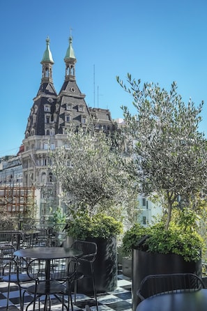Une terrasse avec des sièges extérieurs et une vue sur un bâtiment historique à l’architecture riche et ornée.