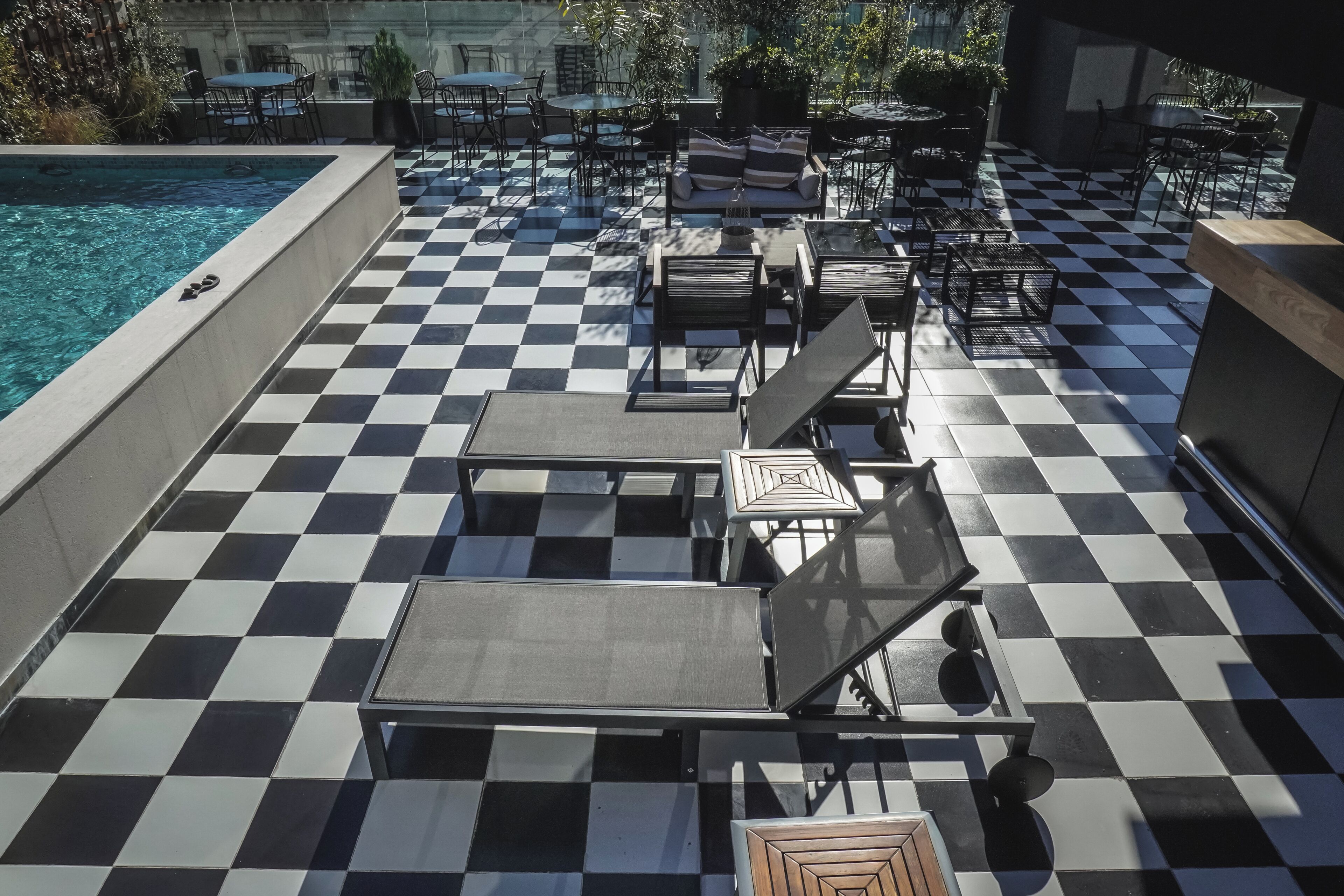 Zona junto a la piscina con suelo a cuadros, tumbonas y mobiliario de exterior.