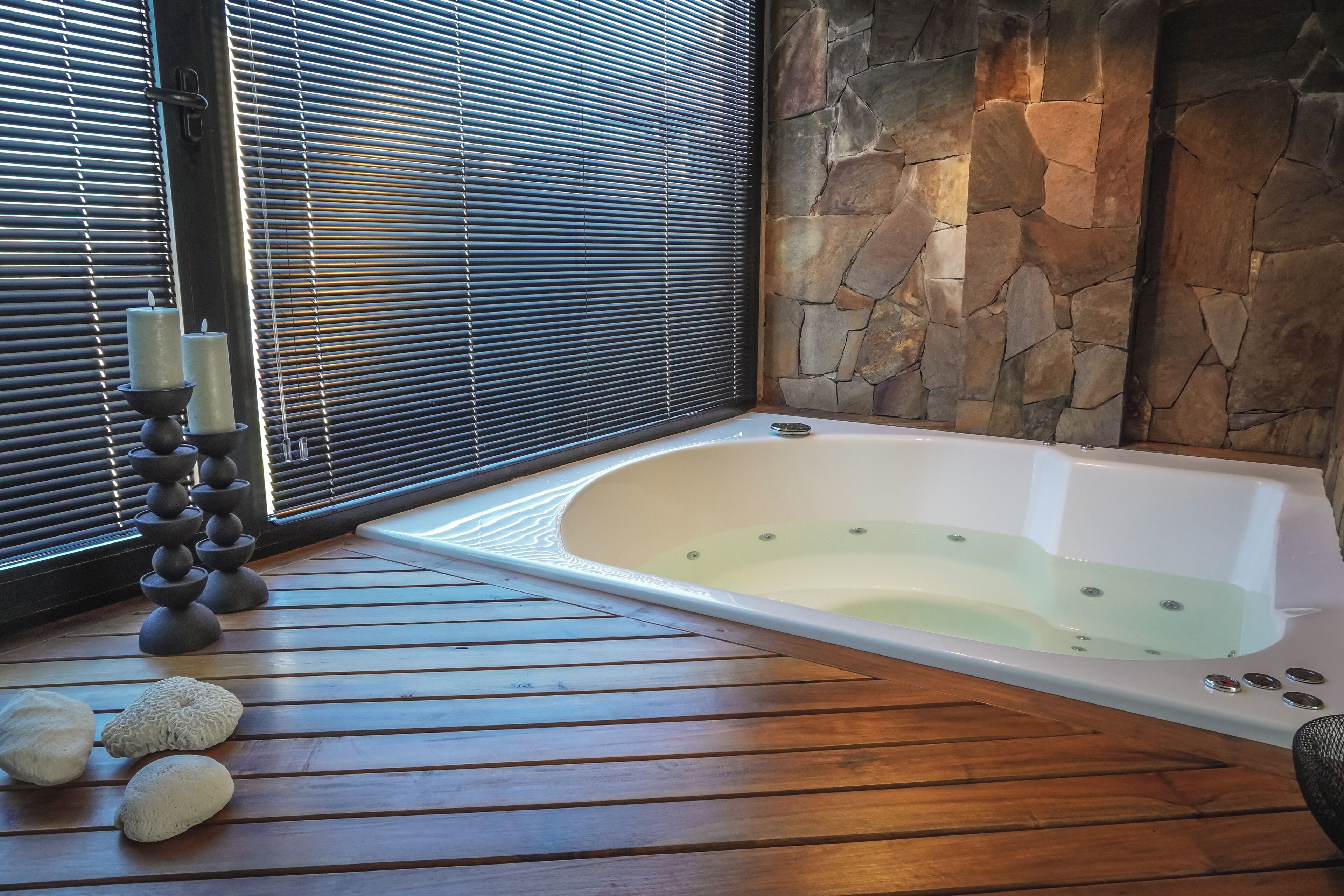 Un cuarto de spa con pared de piedra, piso de madera, bañera y ventana con persianas.