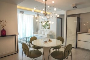 Un espace repas moderne avec une table ronde et des chaises, un lustre et une vue sur un salon comprenant un canapé et un tableau.