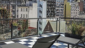 A rooftop terrace with two lounge chairs, a checkered floor, and a view of historic buildings in the background.