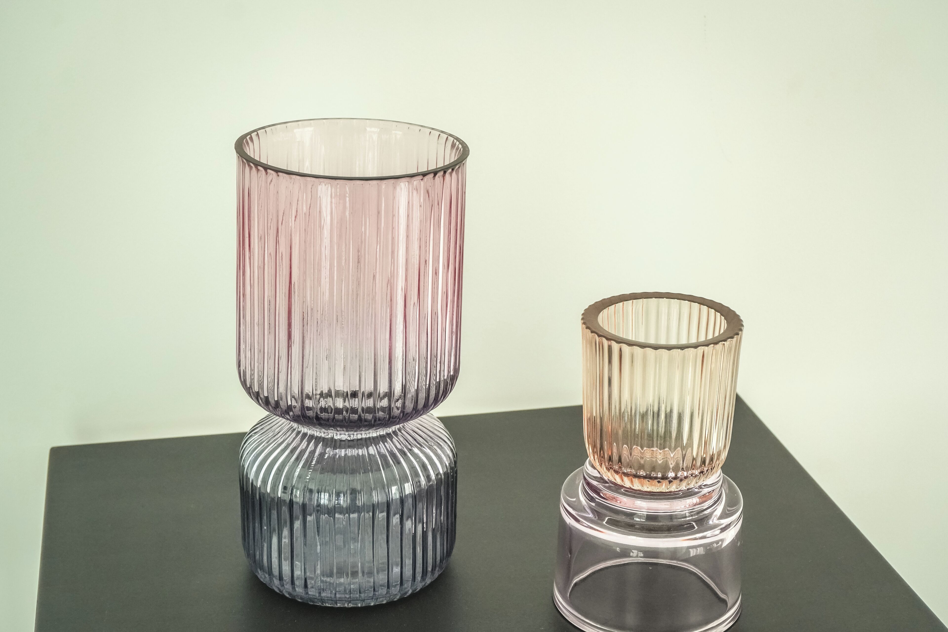 Two glass vases with ribbed textures on a dark surface.