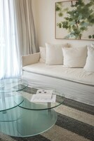 Una sala de estar moderna con una mesa de centro de vidrio, un sofá blanco y un cuadro abstracto enmarcado en la pared.