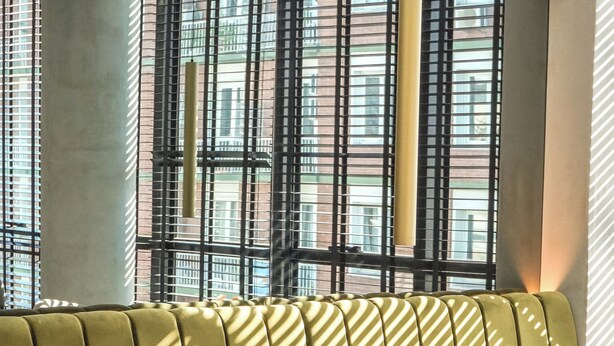 A modern interior with a green sofa, a round table, and a view of buildings through a window with a metal grid. - Aira Apart Hotel Boutique (Buenos Aires)