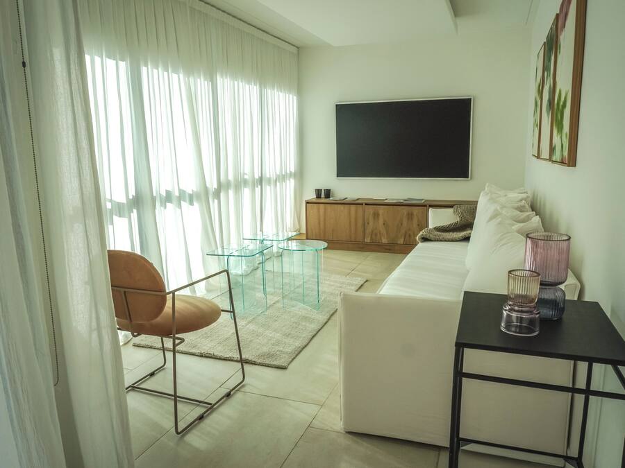 A modern living room with a sofa, a glass coffee table, a chair, a TV, and a painting on the wall.