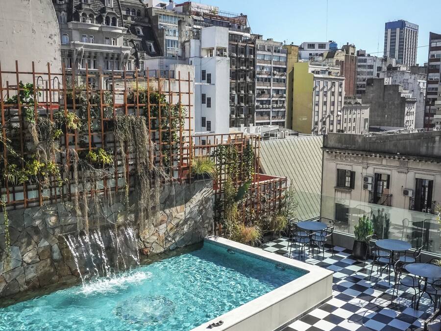 A rooftop pool with a checkered floor, surrounded by a stone wall and plants.
