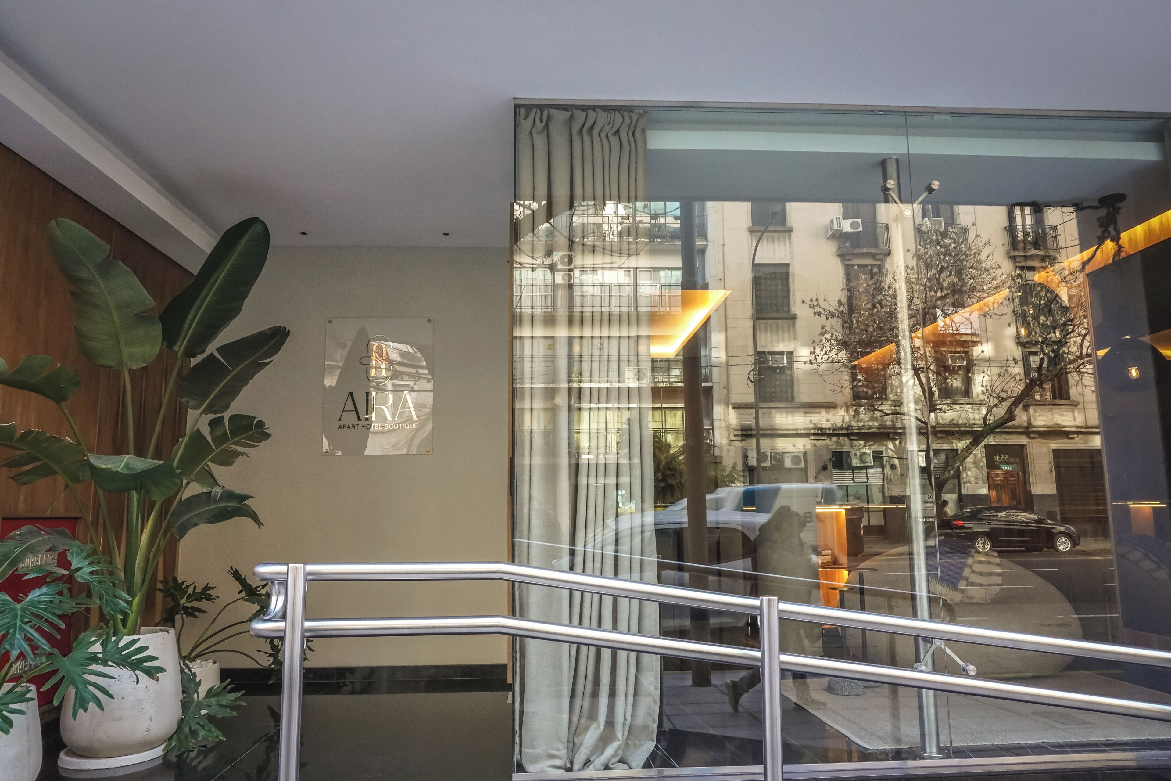 A hotel lobby with a staircase, a sign for 'ARIA APART HOTEL BOUTIQUE,' and a view of the street outside.