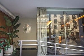 Un hall d'hôtel avec un escalier, une enseigne indiquant « ARIA APART HOTEL BOUTIQUE », et une vue sur la rue.