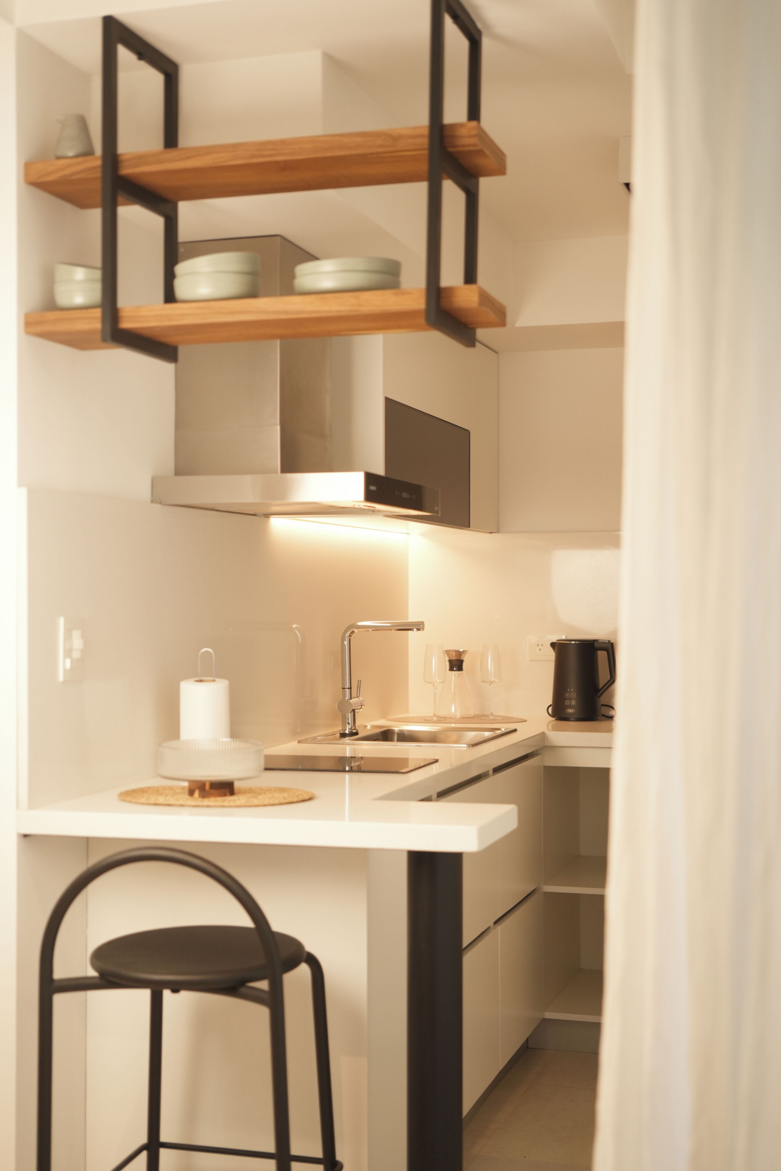 Una cocina compacta con encimera blanca, una silla negra y un estante de madera arriba.