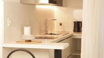 Una cocina compacta con encimera blanca, una silla negra y un estante de madera arriba.
