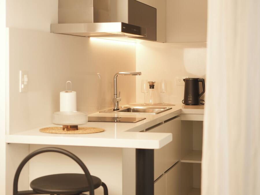 Una cocina compacta con encimera blanca, una silla negra y un estante de madera arriba.