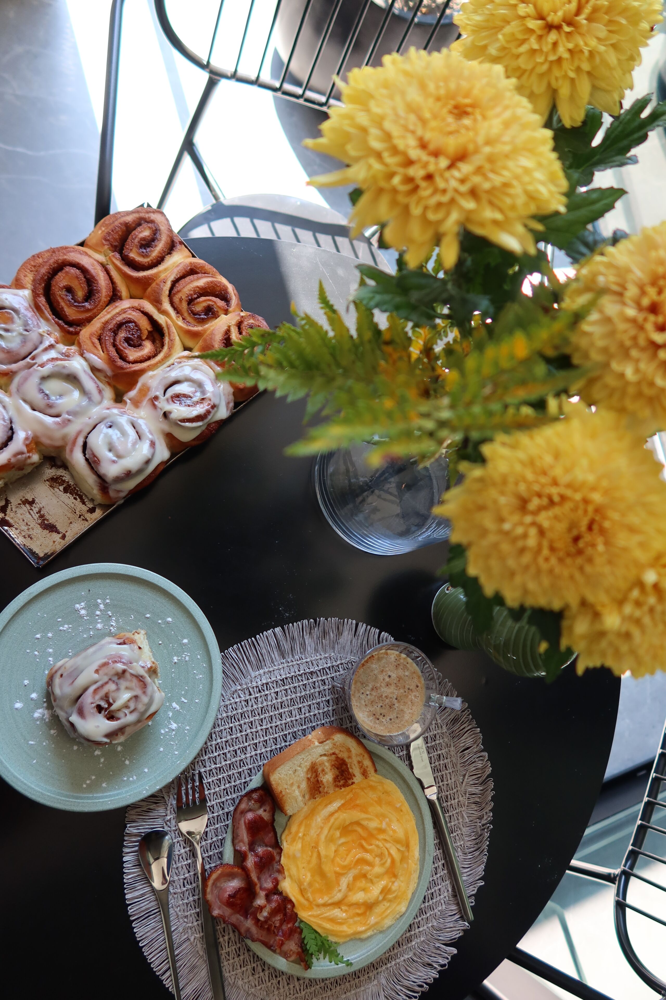 A table with food items, a vase with yellow flowers, and a metal chair.