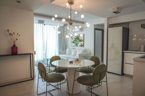 Eine moderne Küche mit Essbereich, inklusive einem runden Tisch mit Stühlen, einer Pendelleuchte und einer Vase mit Trockenblumen auf einem Regal.