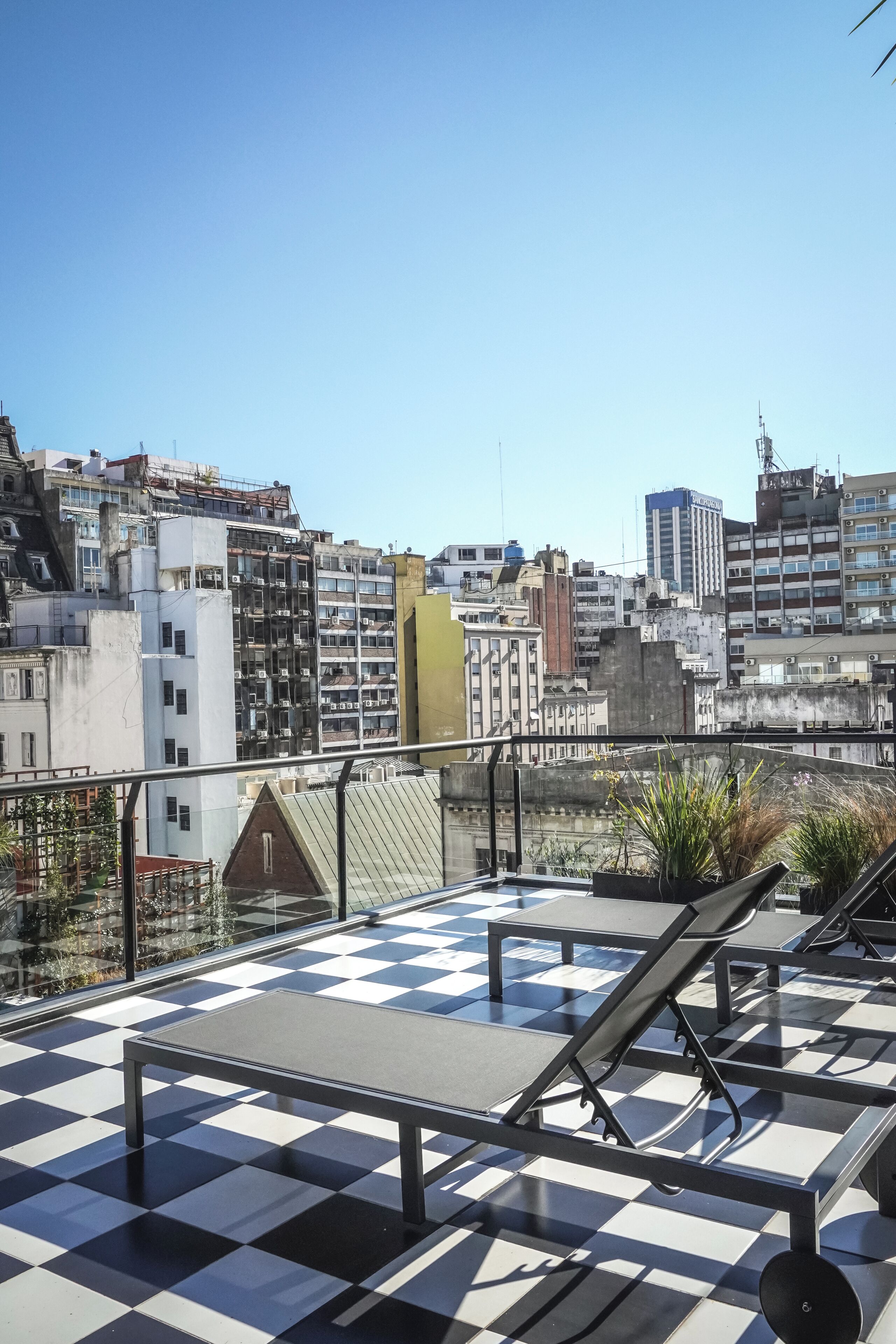 A rooftop terrace with a checkered floor, lounge chairs, and a view of the cityscape.