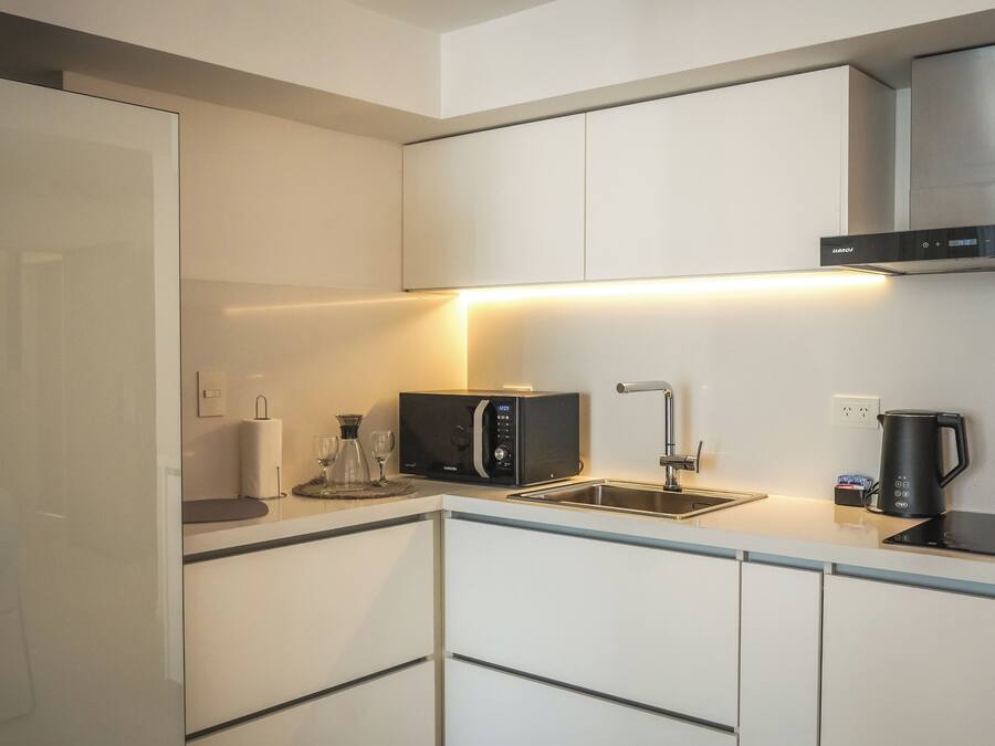A modern kitchen with white cabinetry, a built-in microwave, a kettle, and a sink.