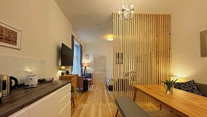 Eine moderne Küche mit Holzarbeitsplatte, ein Essbereich mit einer Bank und ein Wohnbereich mit Fernseher und einer Holzvertellung.