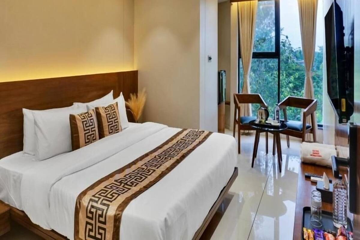 A hotel room with a large bed, a desk with a chair, and a view of greenery through the window.