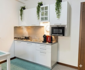 A compact kitchen with white cabinets, a built-in oven, a coffee maker, and a clock on the wall. - Studio Cala di Sole (Imperia)