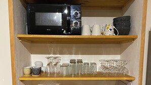 A kitchen shelf with a microwave, glassware, plates, and a small sign. - Cozy vacation rental for 6 people, with a garden in Normandy, near the D-Day beaches (La Luzerne Manche)