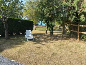 A white plastic chair in a grassy area with trees and a wooden fence. - Cozy vacation rental for 6 people, with a garden in Normandy, near the D-Day beaches (La Luzerne Manche)