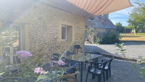 A stone building with a gravel patio, outdoor seating, and a shaded area. - Cozy vacation rental for 6 people, with a garden in Normandy, near the D-Day beaches (La Luzerne Manche)