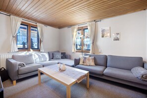 Un salon avec un plafond en bois, deux canapés gris, une table basse en bois et un radiateur.