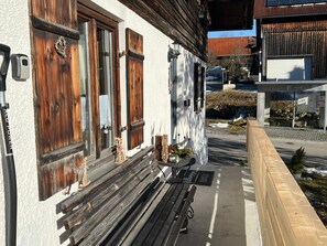 Un bâtiment avec des volets en bois, un banc à l’extérieur et un trottoir dallé.