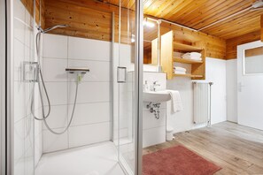 Ein modernes Badezimmer mit einer in Glas eingefassten Dusche, weißen Fliesen, Holzboden und einem roten Teppich.