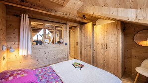 A wooden cabin room with a bed, a window with curtains, a wardrobe, and a mirror reflecting a bear outside. - Holiday Home “L'alpin” with Mountain View (Les Déserts)