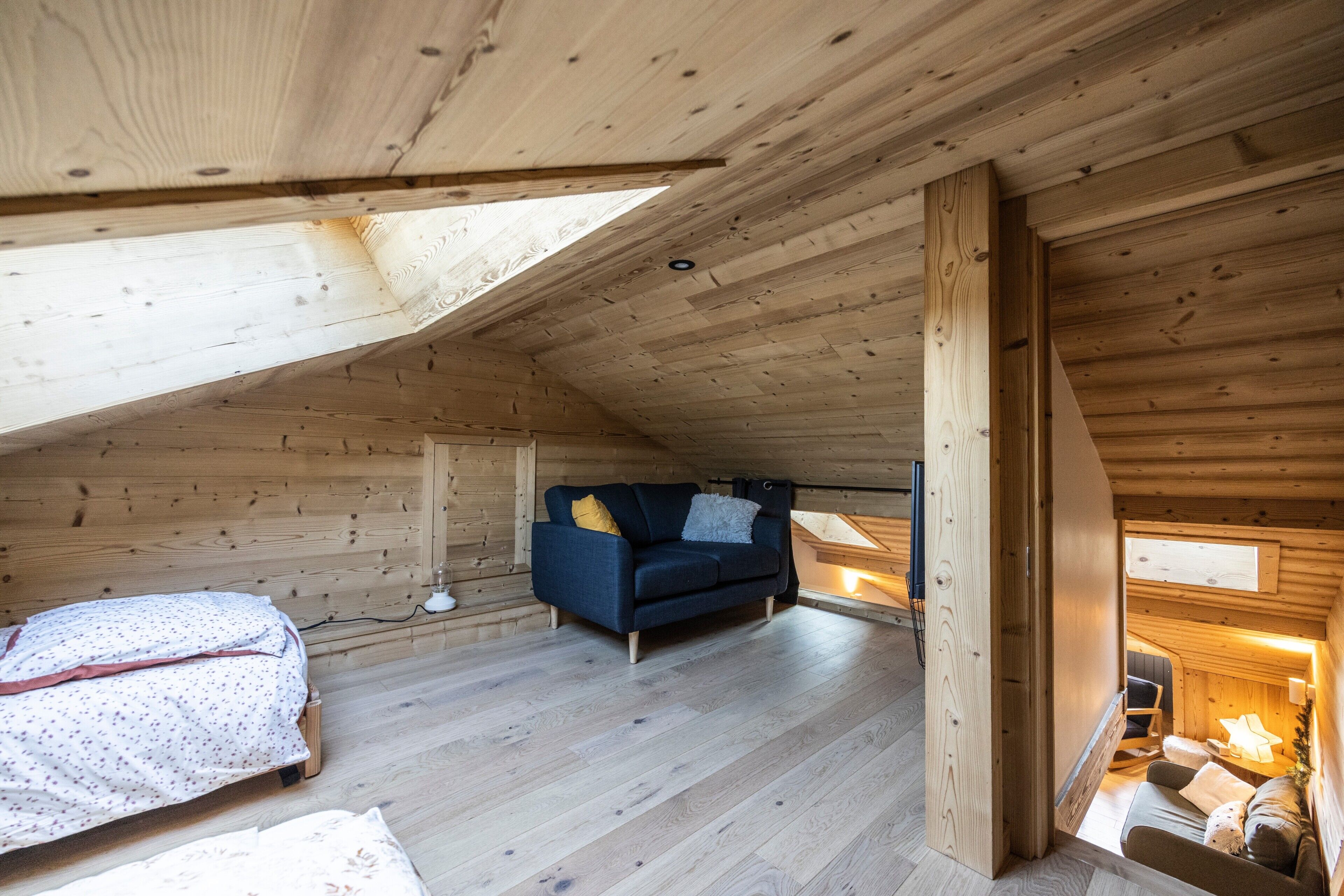Ein Holzinnenraum mit schrägverdeckter Decke, einer Couch, einem Bett und einem kleinen Tisch.